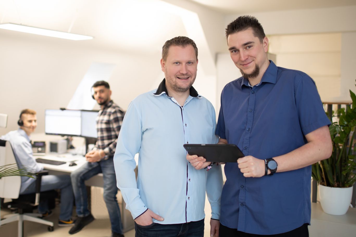 Das Team von xtero im Büro: zwei lächelnde Männer im Vordergrund mit Tablet, zwei Kollegen arbeiten im Hintergrund am Computer