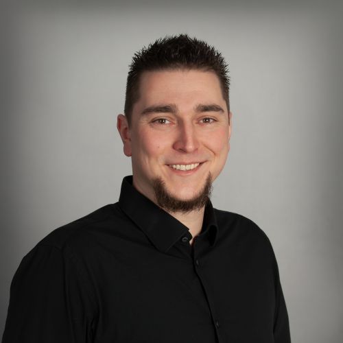 Ronny Reinhardt, Technischer Support bei xtero, lächelt im schwarzen Hemd vor grauem Hintergrund