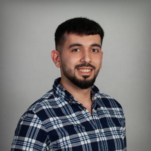 Mohammad Nafiseh, Softwareentwickler bei xtero, lächelt im blau-weiß karierten Hemd vor grauem Hintergrund