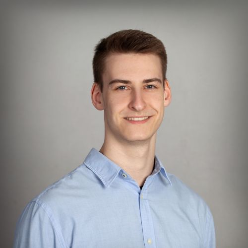 Tim Büchner, Technischer Support bei xtero, lächelt im hellblauen Hemd vor grauem Hintergrund