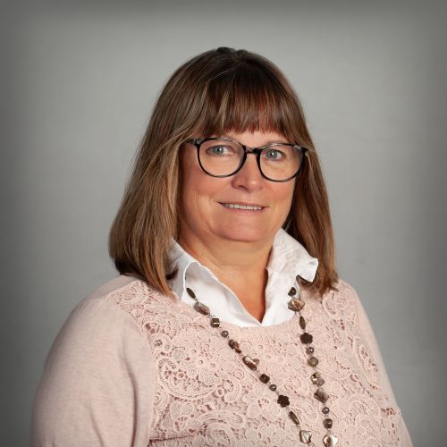 Kornelia Sachse, Büroassistentin bei xtero, lächelt mit Brille im rosafarbenen Oberteil vor grauem Hintergrund